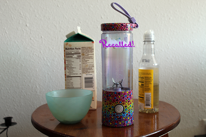 A recalled Lisa Frank Blendjet blender next to oat milk, vanilla syrup, and a bowl of matcha powder in hot water.