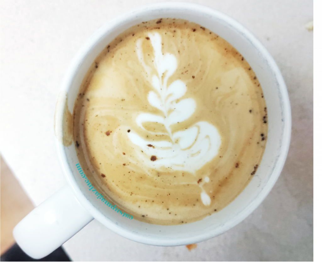 an aerial view of a latte in a white coffee mug with a leaf as latte art