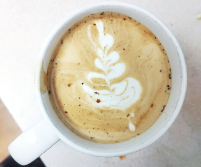 an aerial view of a latte in a white coffee mug with a leaf as latte art