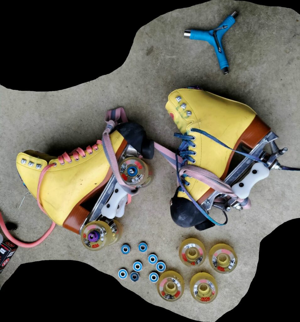 a pair of yellow beach bunny roller skates are sideways on the pavement with wheels, bearings, and a skate tool surrounding them.