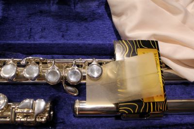 a student flute inside a blue velvet lined instrument case has a cigarette paper between a key for pad cleaning