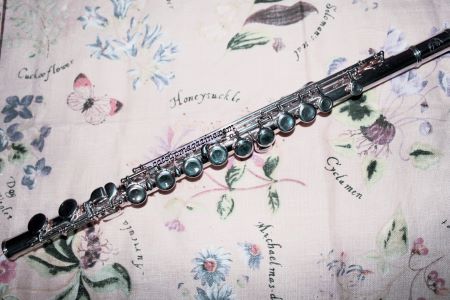 a concert flute rests on top of a woven dresser skirt that has wildflowers imprinted on it