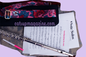 a flute case, concert flute, and two sheets of music are visible from an aerial view. a pink marker is below the papers.