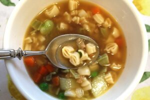 a bowl of dollar sign shaped pasta in vegetable broth appears like "money soup" as a spoonful is being held up in the center