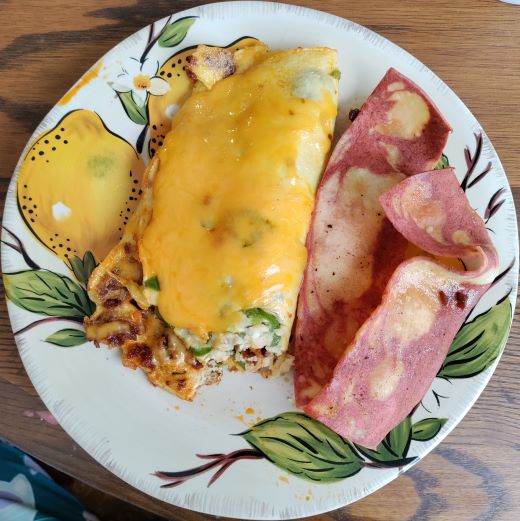 a golden, vegetarian omelette with veggie bacon to the right of it. the food is served on a lemon-printed ceramic plate.