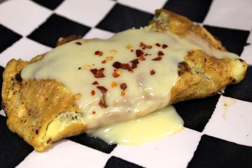 A really good folded omelette with a goldenly crisped surface topped with a cheesy white sauce and red pepper flakes served on a black and white checkerboard ceramic plate.